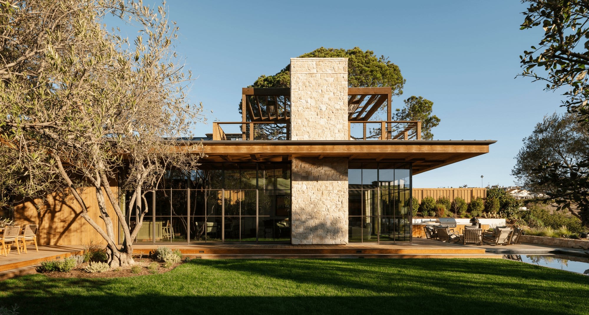 A modern farmhouse with a long run of black steel glazing opening onto a lawn.