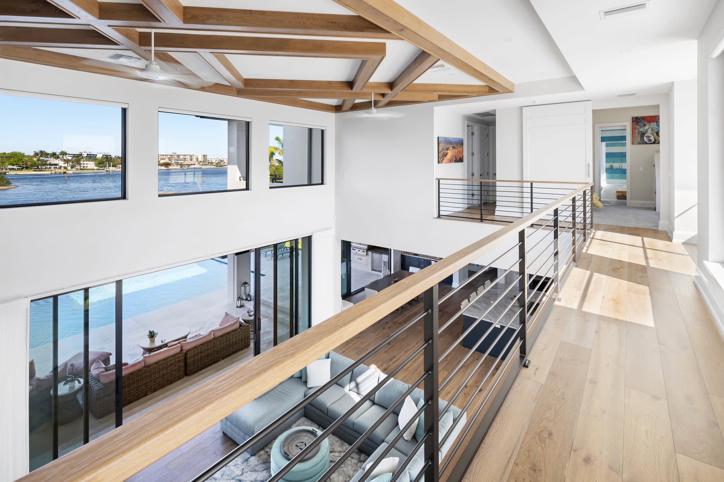A bright upper gallery with a cable rail, looking across tall black-framed glazing to the water beyond.