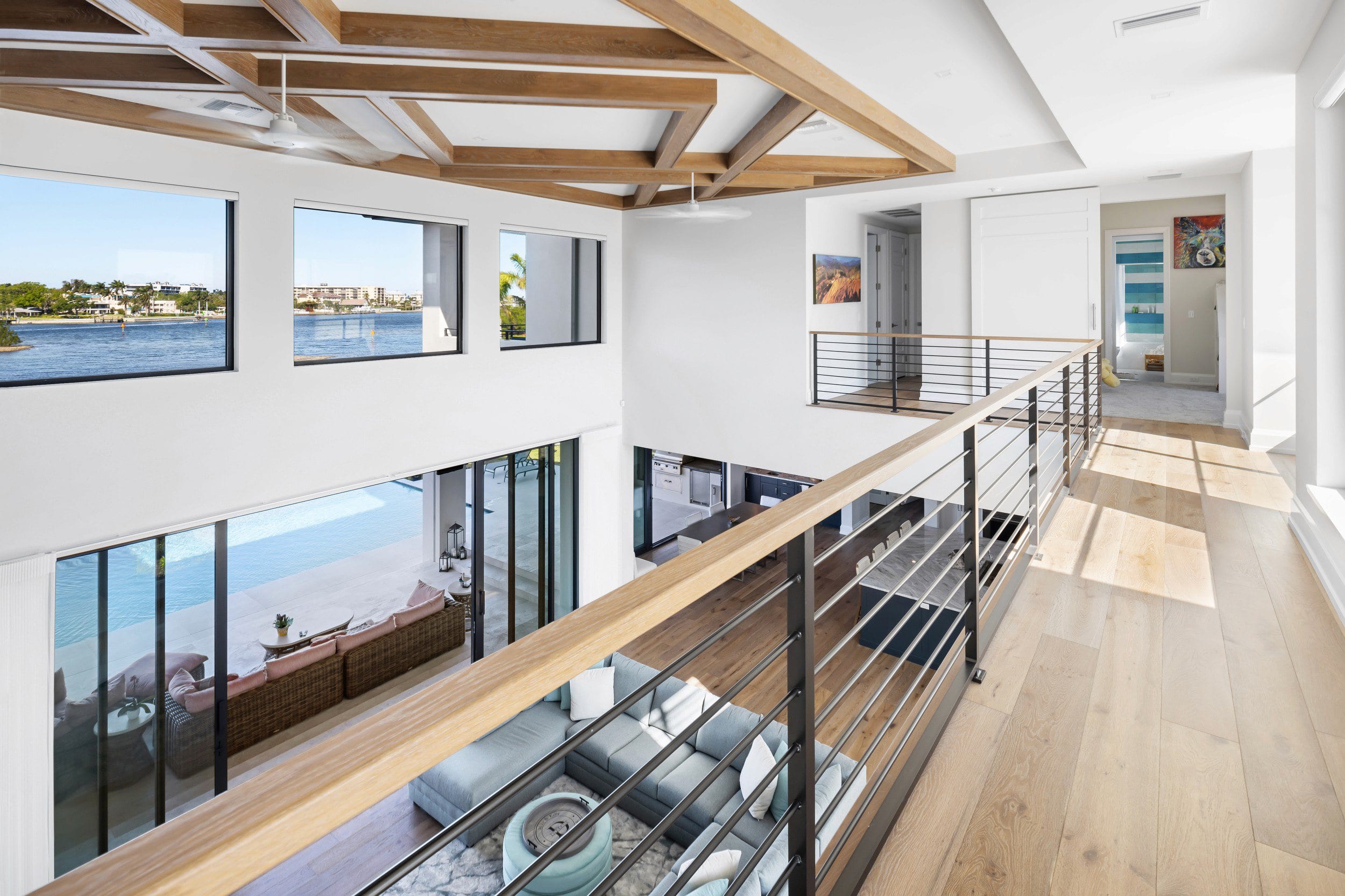 A bright upper gallery with a cable rail, looking across tall black-framed glazing to the water beyond.