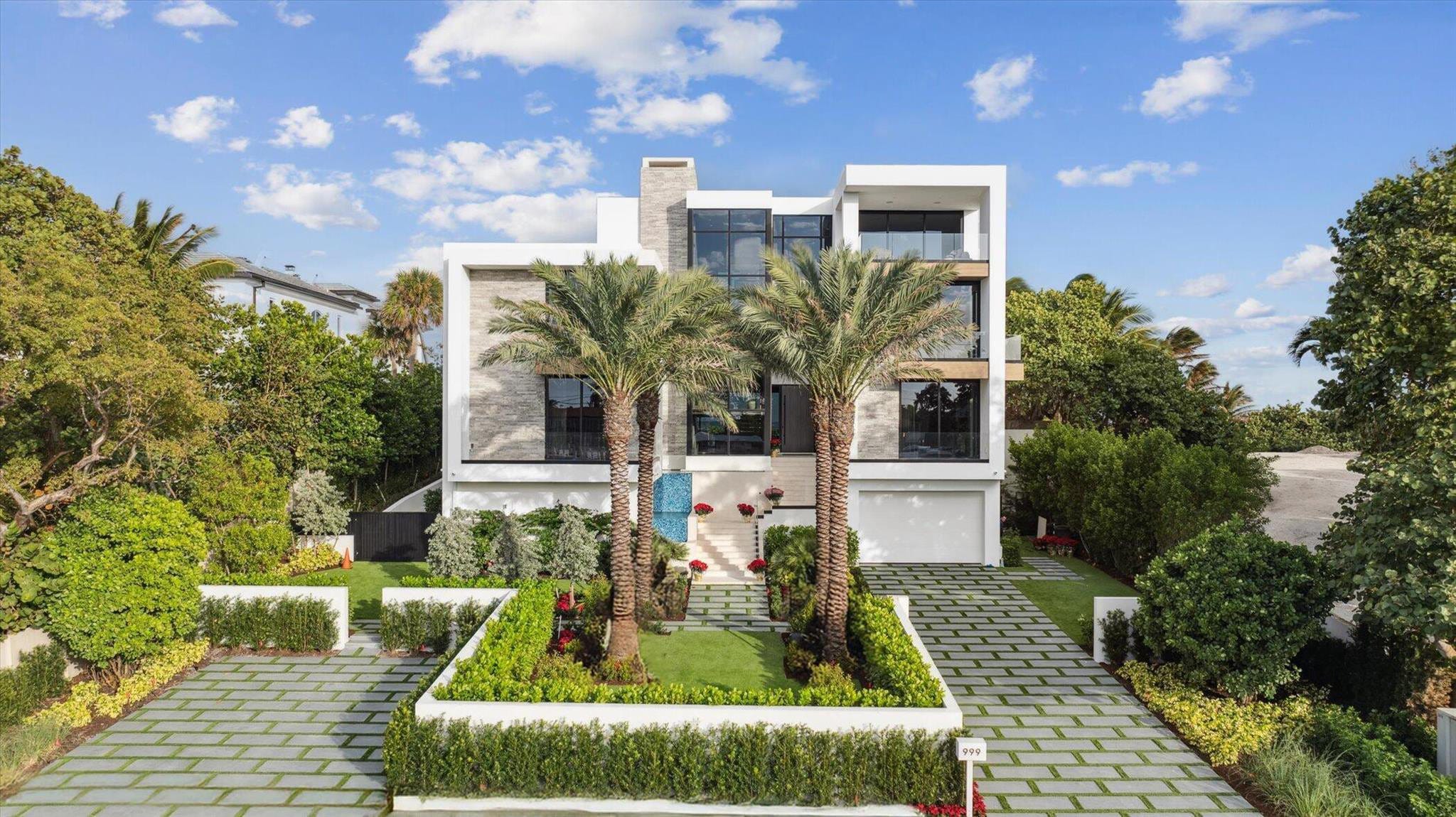 A modern white residence set behind clipped hedging and palms, its tall glazed openings framed in black.