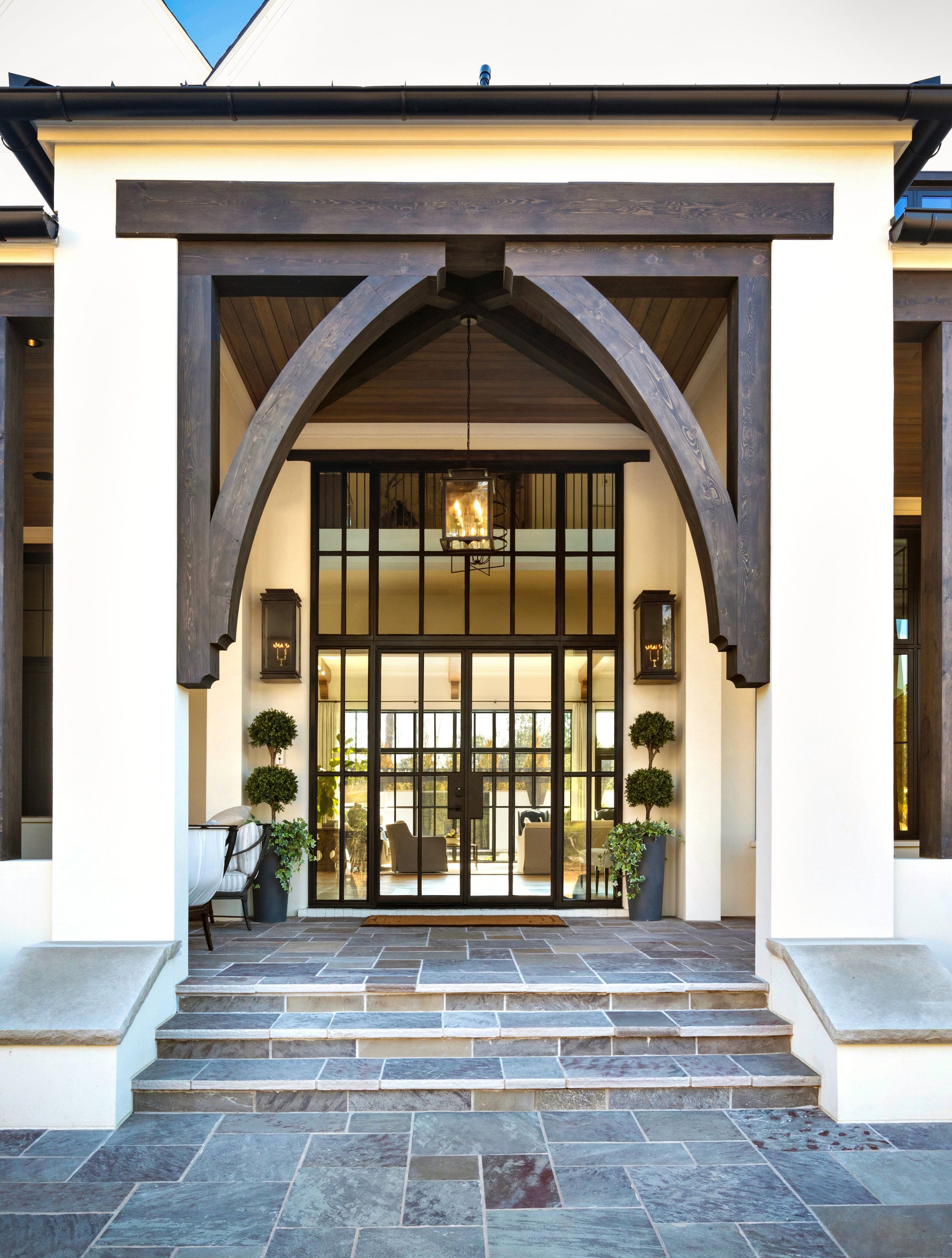 Covered entry with heavy timber trusses above a tall steel-framed glazed door and slate steps.