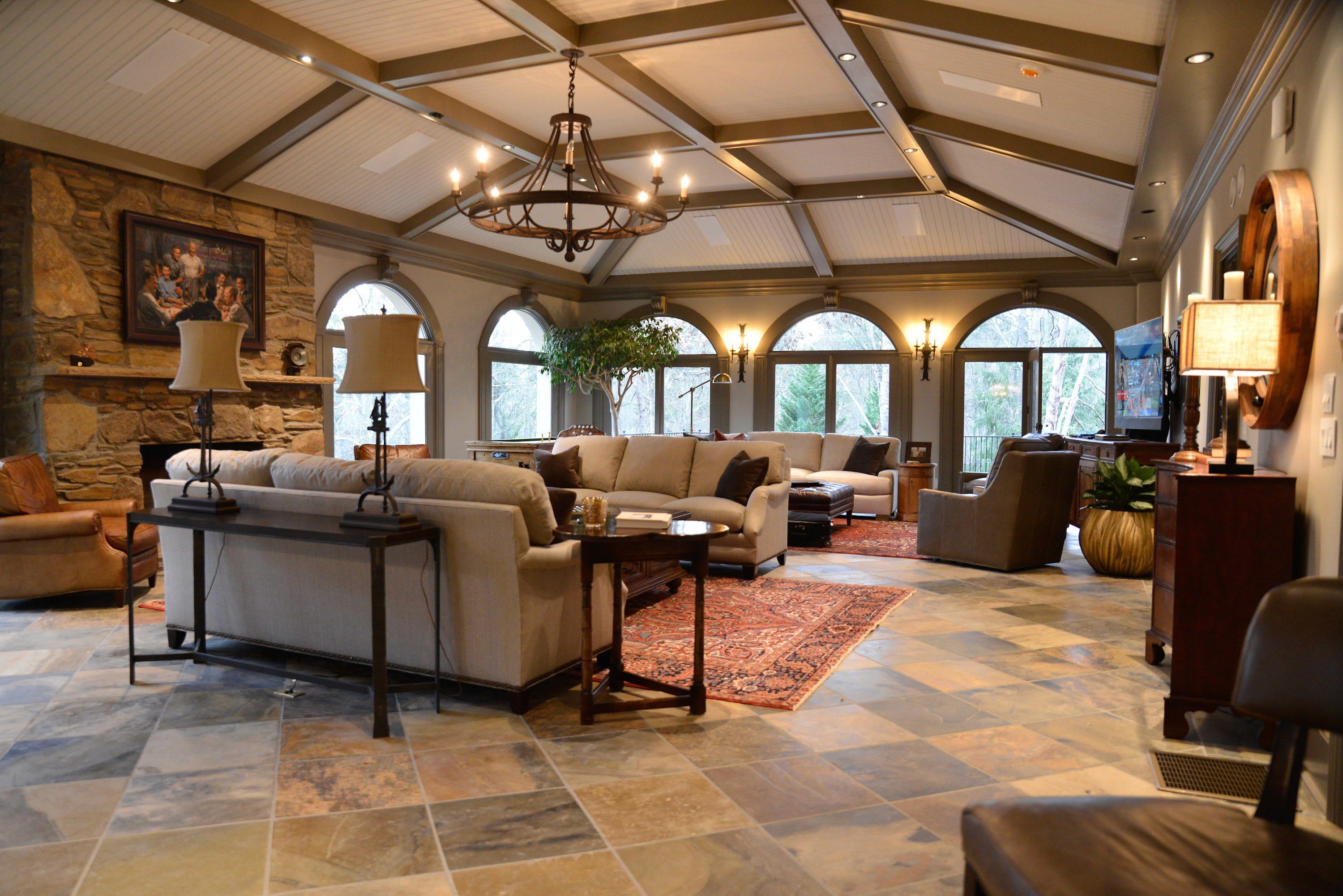 A great room under a coffered timber ceiling, lit by a run of arched windows along the far wall.