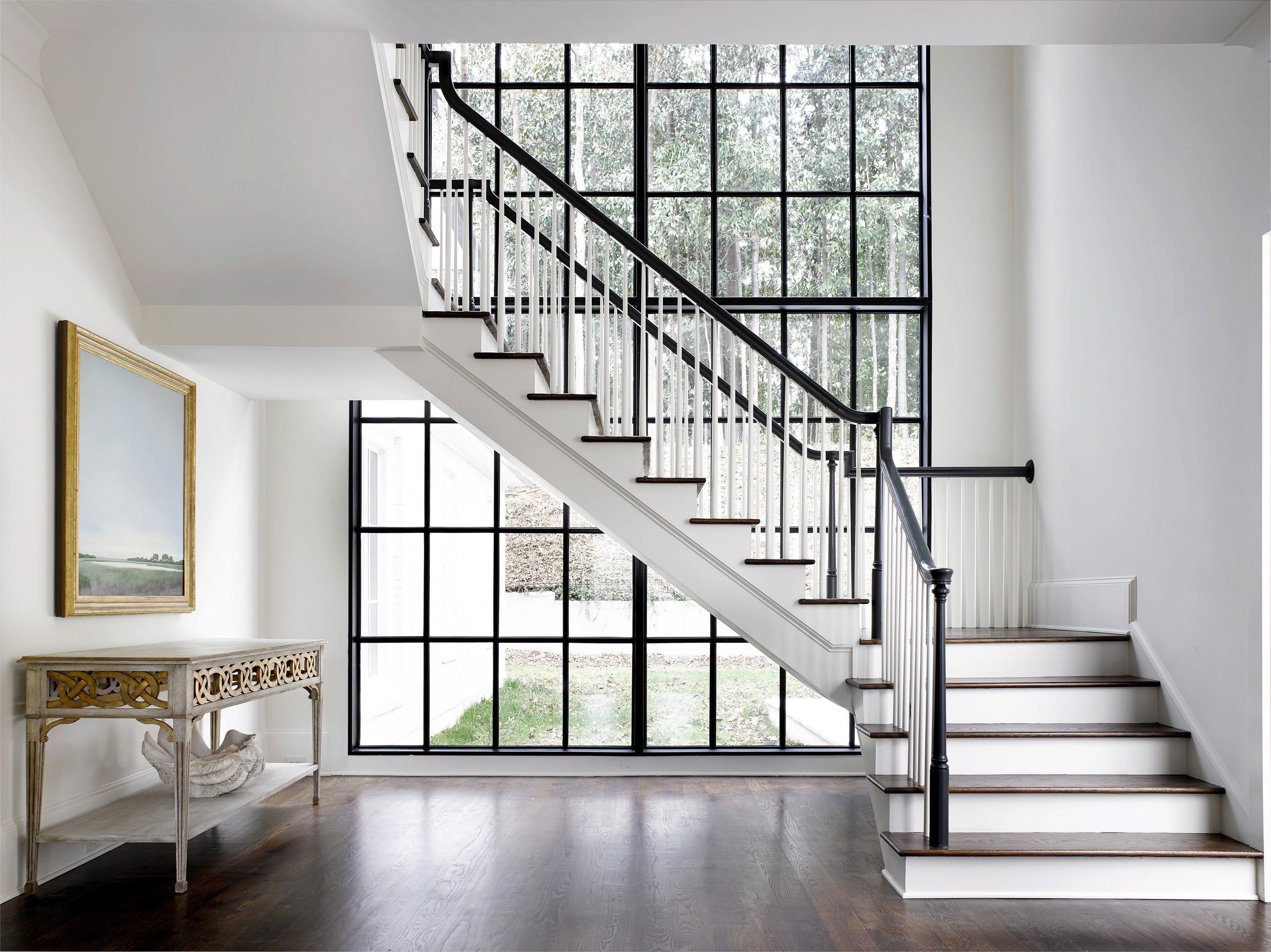 A tall black steel window with a fine gridded muntin pattern, running the full height of a white stair hall.