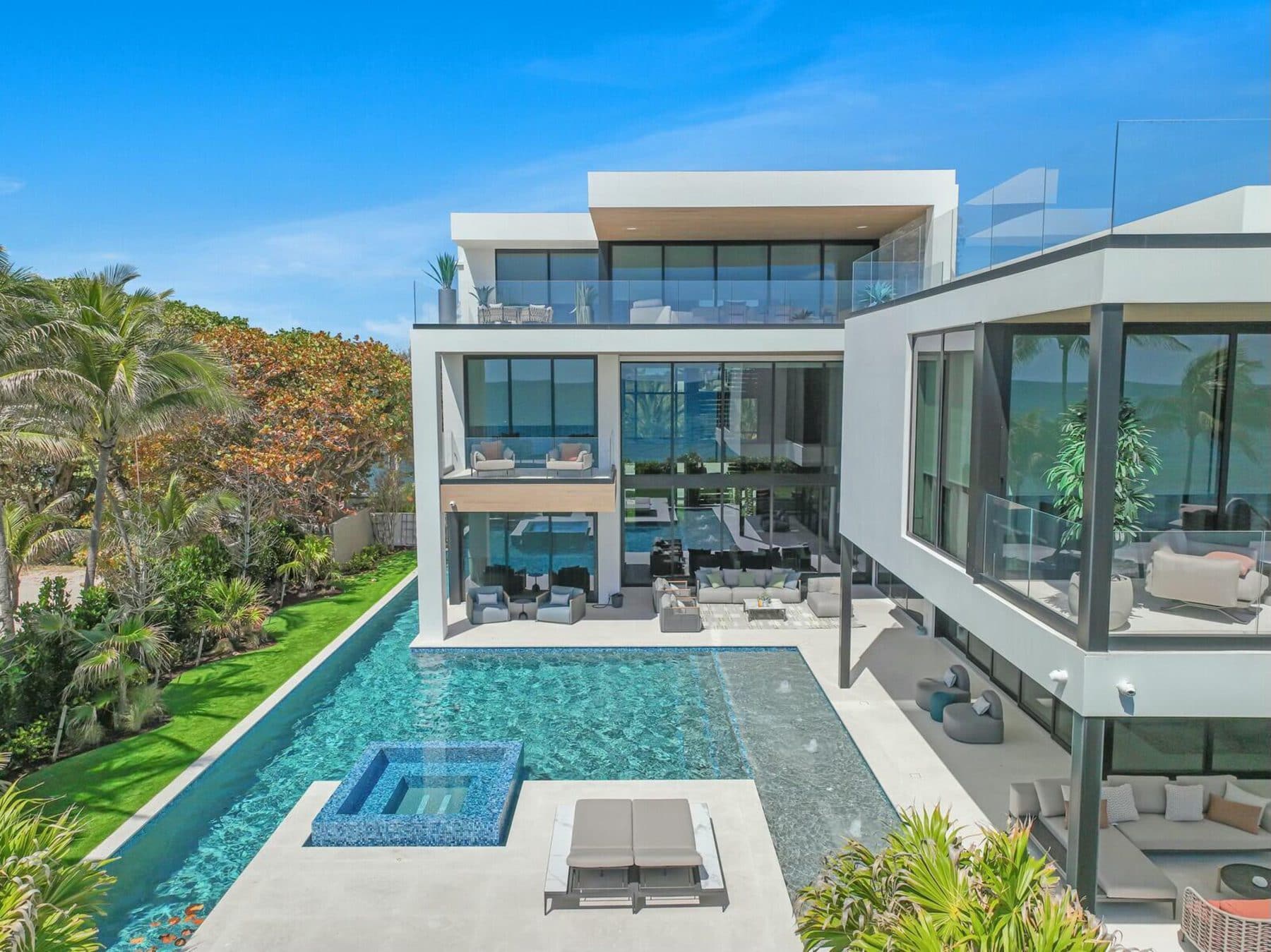 A modern multi-storey residence seen from above, its glazed facades facing a long pool and garden.