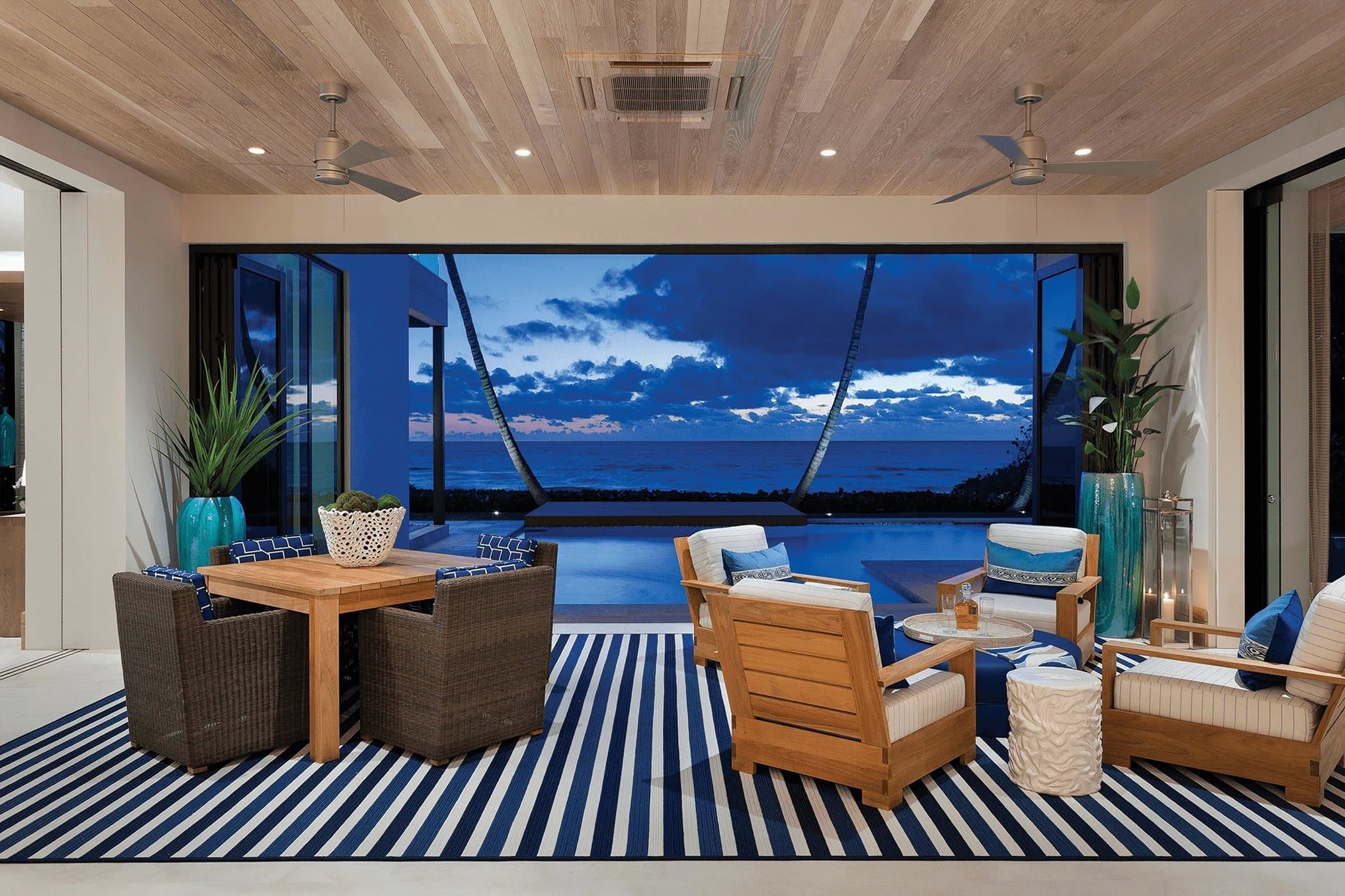 A wide opening from a timber-ceilinged lanai onto a pool and open water at dusk.