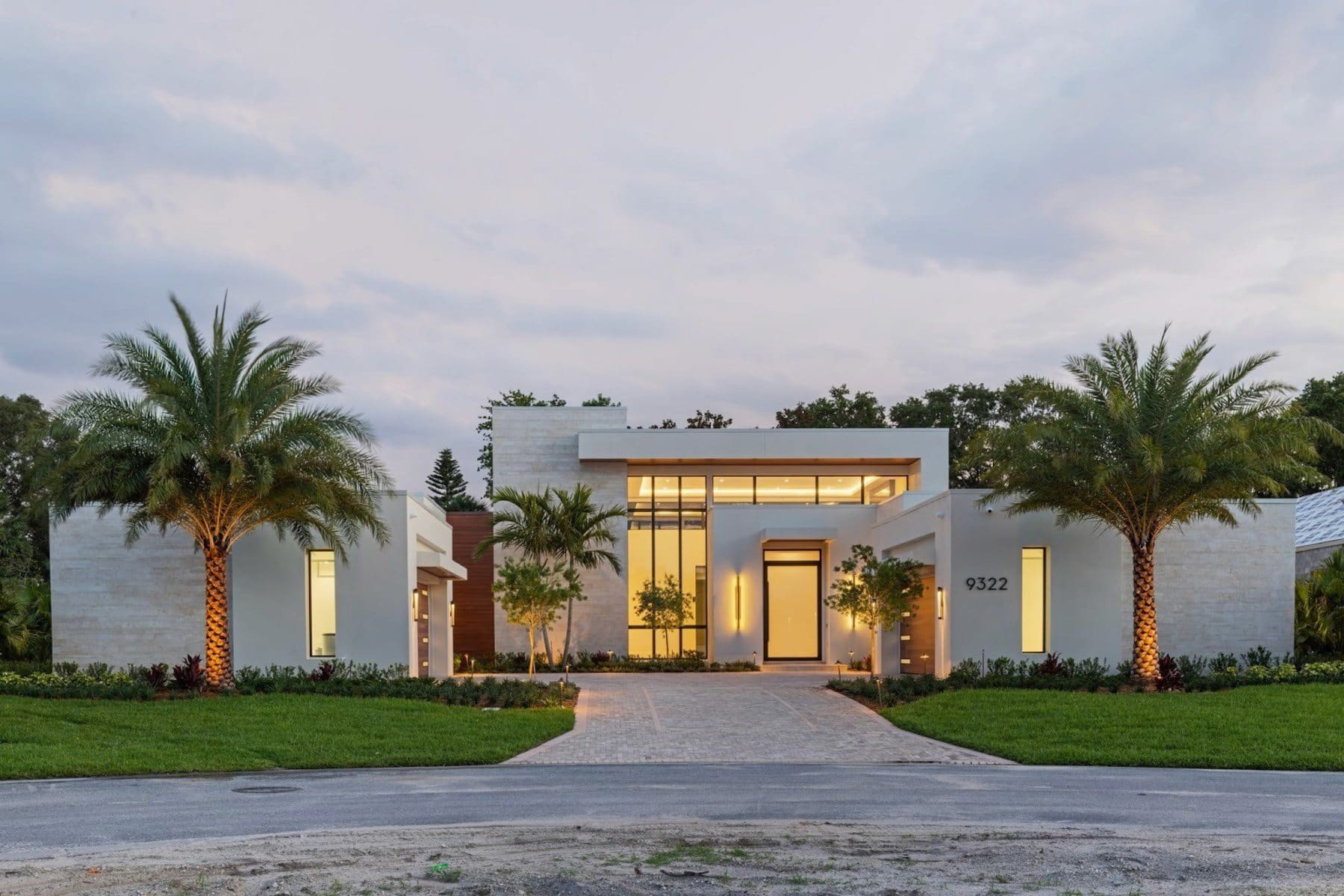Modern custom residence at dusk in Windermere, Florida, its glazed entry and floor-to-ceiling windows lit from within, framed by palms.
