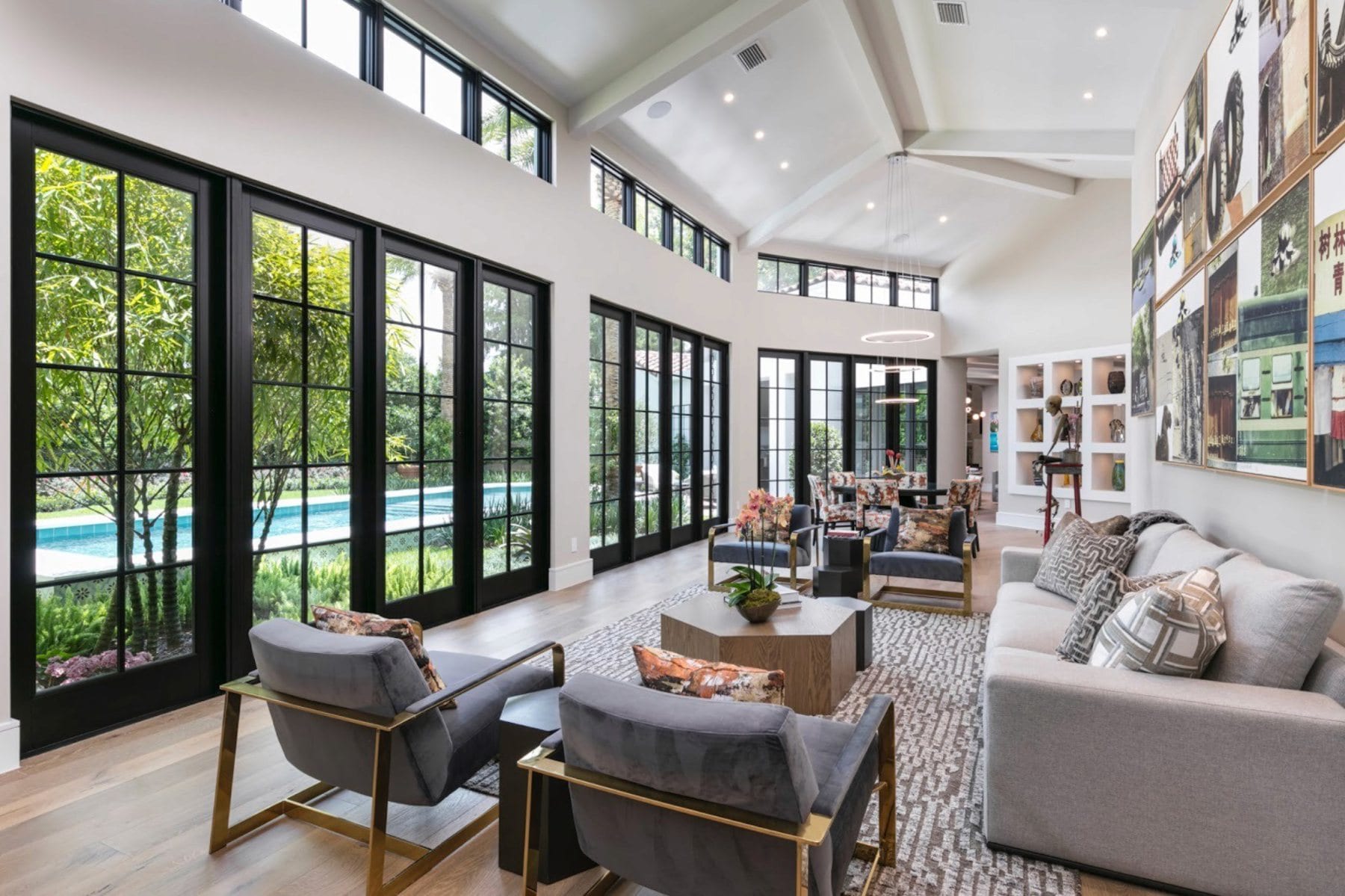 Long living space lined with tall black-framed floor-to-ceiling windows looking out onto greenery and a pool.